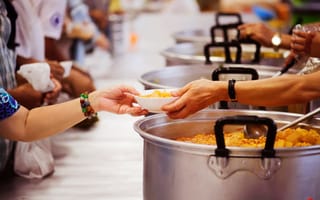Volunteers spoon food into bowls and serve it to people.